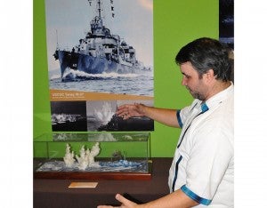 Junto a cada diorama Roberto Danilov tiene poster con las escenas que está recreando. En esta por ejemplo se ve las columnas de agua que saltan junto a un barco que es bombardeado desde el cielo.